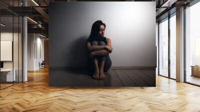 Young sad woman with beatings on the body, sitting disheveled on the floor in the room. There is a light wall in the background.Human trafficking, sexual slavery concept. Copy space Wall mural