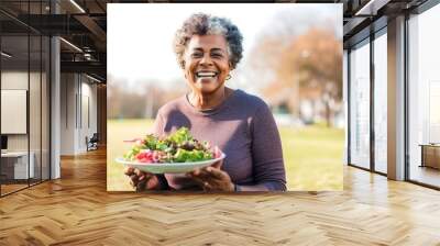 African old woman eating healthy salad after exercising in the park in sportswear during the day Wall mural