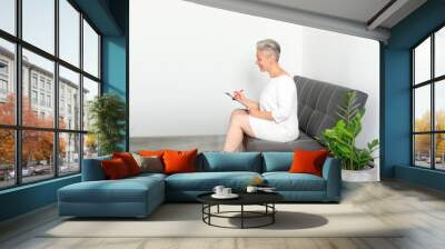 Mature woman at a consultation in a medical clinic fills out a questionnaire while sitting on a sofa. Wall mural