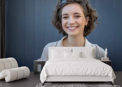 Portrait of a young woman with curly hair on a gray wall background. Beautiful girl looks into the camera. Wall mural