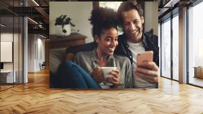 Look at these messages with me. a happy young couple using a cellphone together while relaxing on a couch at home. Wall mural