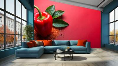 A vibrant red pepper garnished with seasoning and a green leaf on a red background Wall mural