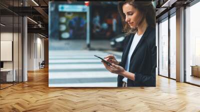 Close-up female hands holding smart phone screen on background of street crosswalk. Young businesswoman using mobile device standing on city road Wall mural