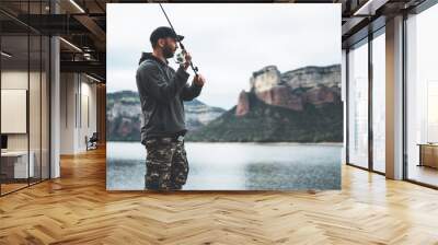 fisherman enjoy hobby with fishing rod on lake, person catch fish on background mountain, holiday relaxation fishery concept Wall mural