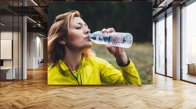 Girl quenches thirst after fitness. Smile person drinking water from plastic bottles relax after exercising sport outdoors, woman isolation training in forest nature drink water after jogging Wall mural