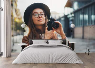 Hobby photographer concept. Outdoor lifestyle portrait of pretty young woman in sun city in Europe with camera travel photo of photographer in glasses and hat take photo copy space mockup Wall mural