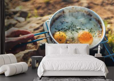 person cooking fried eggs in nature camping outdoor, cooker prepare scrambled omelette breakfast picnic on metal stove, tourism recreation outside; campsite lifestyle Wall mural