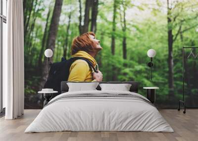 smiling tourist traveler with backpack into road at summer green forest, girl hiker in yellow hoody  Wall mural