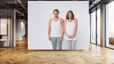 pregnant woman and man in sportswear on white background. The girl holds her stomach with her mouth wide open and a smile on her face Wall mural