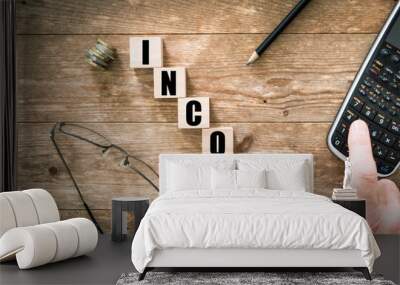 Blocks with black letters saying Income on wooden background with hand on calculator Wall mural