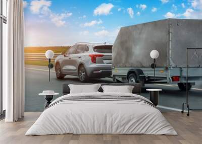 car with a trailer covered with an awning is driving along the highway in the sky clouds and sunset. Wall mural