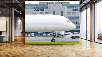 Freight cargo airplane in the parking lot of the airport, against the background of the cargo terminal of the aerodrome building. Wall mural