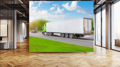 Heavy truck with a white trailer rushes along the road among green trees and meadows, sunset clouds are beautiful in the sky. Wall mural