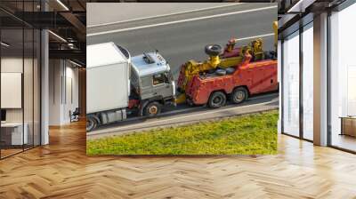 Powerful heavy duty big rig mobile tow semi truck with emergency lights and towing equipment prepare to tow broken white semi tractor standing out of service on the highway side. Wall mural