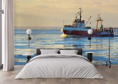 Frozen fishing vessel in coming back to the port at the sunset Wall mural