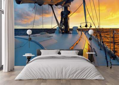 White yacht sailing in an open sea at sunset. A view from the deck to the bow, mast, sails. Epic cloudscape. Dramatic sky with glowing golden clouds after the storm. Racing, sport, leisure activity Wall mural