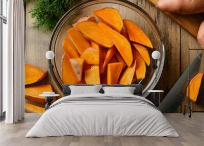 A top-down view of a wooden kitchen countertop with freshly cut sweet potato wedges soaking in a large glass bowl of water. Wall mural