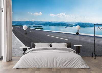 Asphalt highway road and lake with mountains nature landscape on a sunny day. Beautiful coastline in summer season. Wall mural