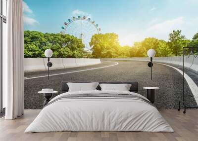 Asphalt road and ferris wheel playgrounds with green tree in the city park Wall mural