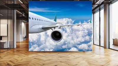 Commercial airplane flying above blue sky and white clouds. Wall mural