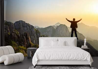 Hiker is standing on a rock with raised hands and enjoying sunrise Wall mural