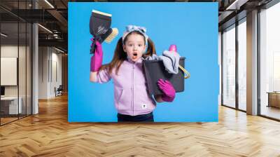 A shocked girl sees the amount of cleaning that awaits her. Surprised child holds bucket from mop with liquid, sweep and dustpan, rubber pink gloves, daughter helps mom with household chores. Wall mural