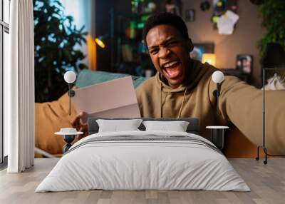 African American man receiving news screaming in celebration while holding stack of papers in hands t official documents or personal writing, it's clear that he is overjoyed by his accomplishment. Wall mural