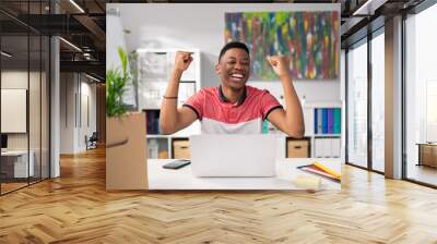 Ambitious hardworking handsome man of African American descent sitting in office in front of computer got good news, won a tender, got a promotion, happy raises hands in air, win, victory Wall mural