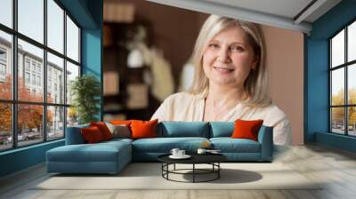 Headshot portrait positive mature woman with healthy smile standing on background of cozy living room, happy middle-aged lady looking to camera, posing for photo at home, enjoying leisure time. Wall mural