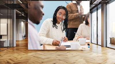 Woman in glasses with dark complexion and pigtails sits in office at work in conference meeting with colleagues, discussing business project, filling out documents, drinking coffee, corporate work Wall mural