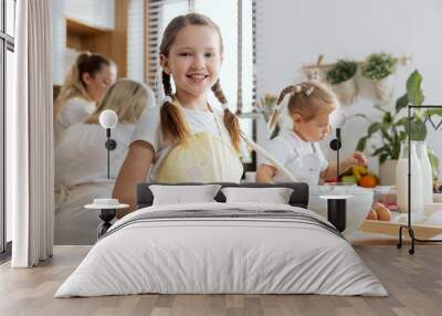 Young helper daughter kneading dough looking at camera smiling. In background gandmother and mother silouhettes talking. Family baking cooking domestic bread pizza pasta having fun together. Wall mural