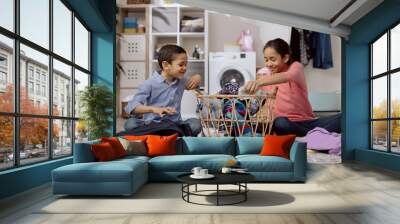 Younger brother and sister sort the clothes to be washed by appropriate colors, spending time in the laundry room doing household chores. Wall mural