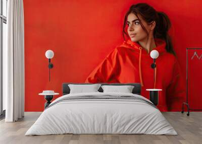 Female fitness model in a red hoodie standing confidently, isolated on a bright red background Wall mural