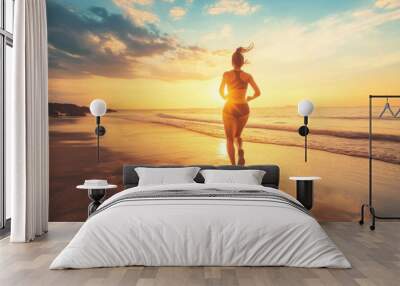 Sporty woman running along sandy beach at sunset Wall mural