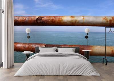 A rusty fence with a blue sea in the background.Rusty iron railing, beautiful sea and sky landscape view between rusty railing gap. Wall mural