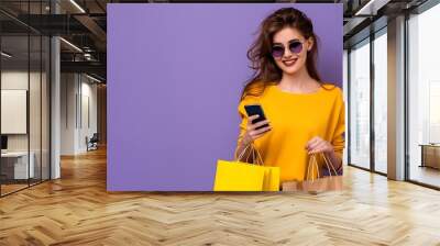 Young woman in sunglasses, holding shopping bags, using mobile phone, purple background, copy space for banner. Wall mural