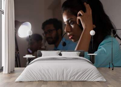 An Indian Bengali brunette young woman/telecaller in office wear is sitting on a office table in a working mood in a corporate office/bpo/call center with others in a group. Indian corporate lifestyle Wall mural