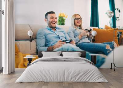 young couple having fun and laughing while playing video games in modern living room Wall mural