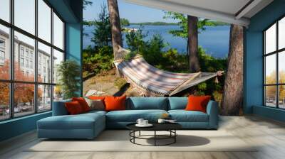 Summer on the lake. Colourful Empty hammock between two trees with the view of the blue water. Wall mural