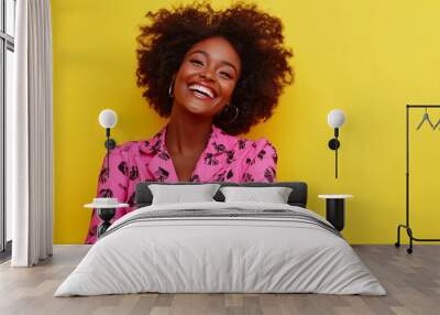 Happy optimistic african american woman in colorful pink clothes laughing isolated on yellow background. Wall mural