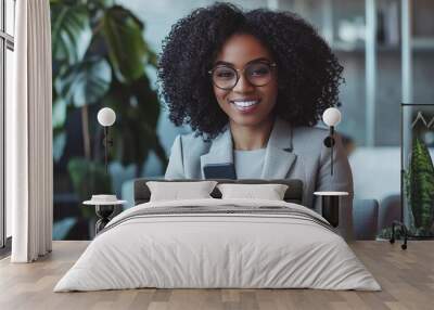 Portrait of a beautiful confident businesswoman using a laptop computer holding a mobile phone sitting in a modern office. smiling african american freelancer working online from home. Wall mural