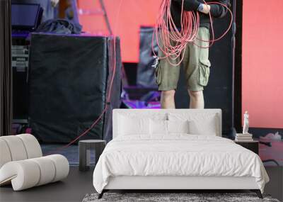 Worker gathering cables on stage. Electrician working on a stage. Man working at event. Technician preparing the lighting wiring for a musical show on stage. Wall mural