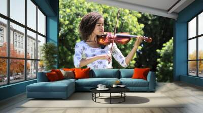 young woman with curly hair playing violin outdoors Wall mural