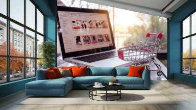 Online shopping concept - shopping cart or trolley and laptop on table Wall mural