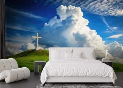 A solitary white cross stands tall on a lush green hill, surrounded by a dramatic backdrop of fluffy white clouds against a serene blue sky. Wall mural