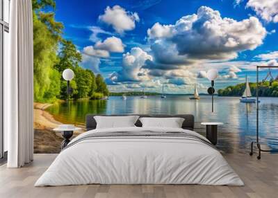 Serene summer afternoon at a tranquil lake beach surrounded by lush green trees, sailboats drifting peacefully, and a soft blue sky with puffy white clouds. Wall mural