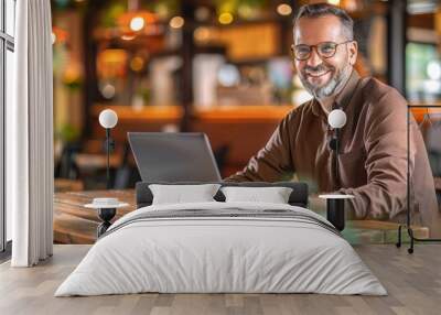 Man working on laptop, freelancer with computer in cafe at table, man in glasses smiling looking in camera Wall mural