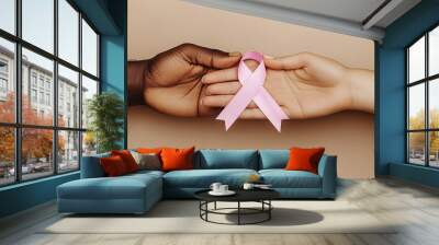 side by side black man and caucasian woman hands  holding together a pink ribbon in support for breast cancer month . Wall mural