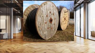 Two wooden coils with electric black cables outdoors in a field under a blue sky Wall mural