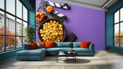 A bowl of popcorn, remote control, and Halloween decorations arranged on a purple background for a spooky movie night Wall mural